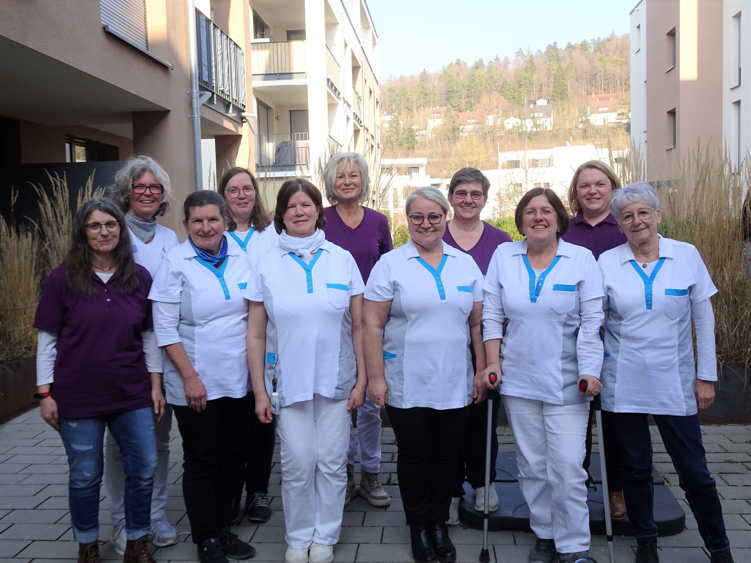 Eine Gruppe von Frauen in weißen und lila Uniformen steht draußen vor einem Gebäude.