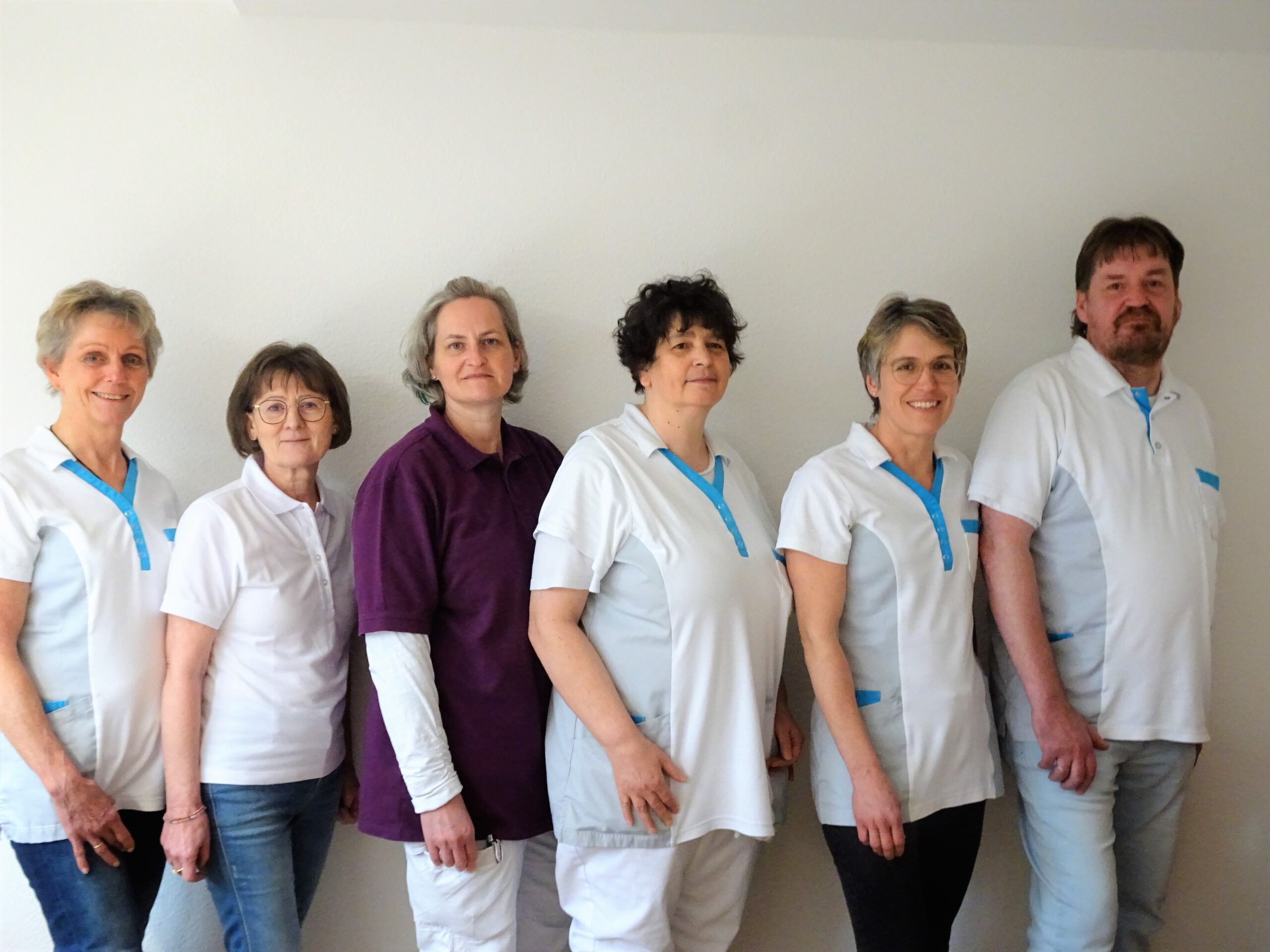 Sechs Personen in weißer Arbeitskleidung stehen nebeneinander vor einer weißen Wand.